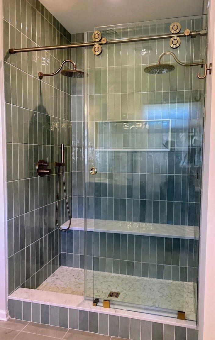 Walk-in shower with green vertical stacked tile, dual rain heads, bench, niche, and brushed gold barn-style glass door