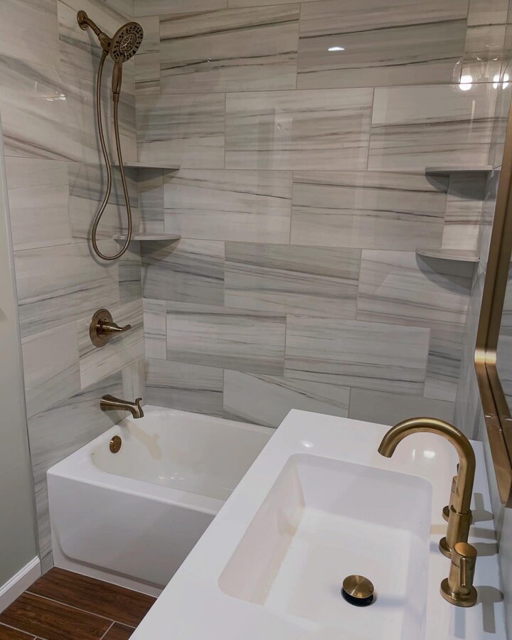 Bathroom with gray wood-look plank tile surround, brushed gold fixtures, soaking tub, and white integrated sink vanity