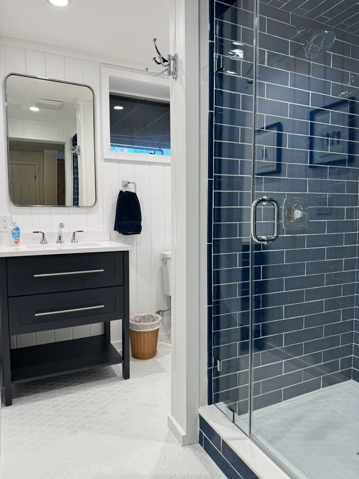 Bathroom with navy subway tile shower and glass door, navy vanity, white shiplap, and hexagon floor tile