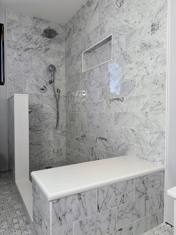 Marble subway tile walk-in shower with bench, pony wall, niche, and basketweave floor tile