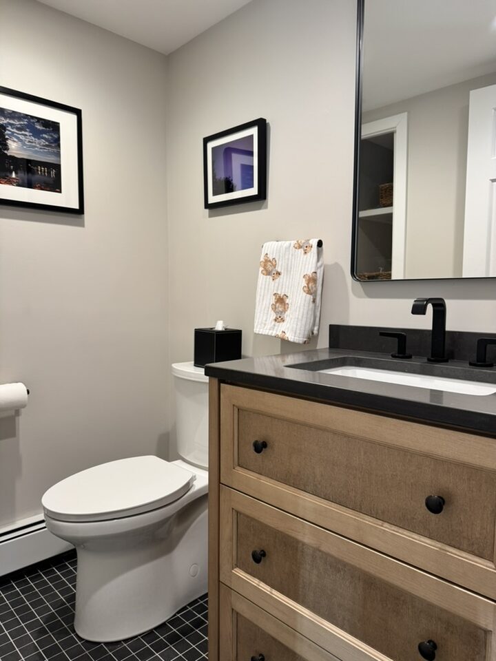 Powder room with oak vanity, dark countertop, matte black faucet, and black mosaic floor